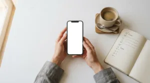 Mãos segurando smartphone sobre mesa branca com caderno e café representando negociação de dívidas